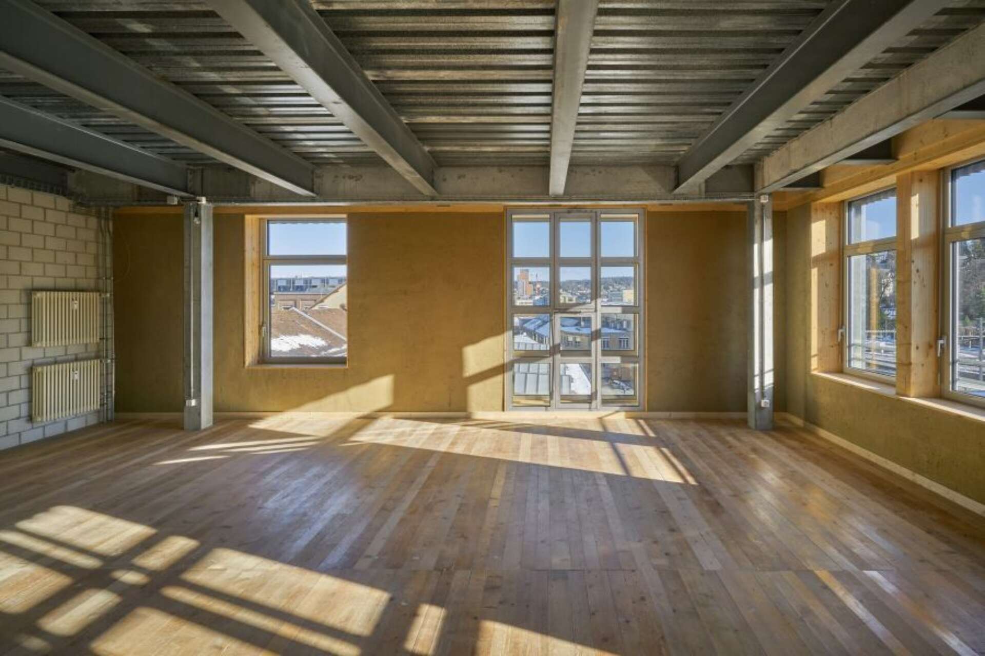 Innenraum der Aufstockung: Wiederverwendete Holzdielen am Boden, wiederverwendete Stahlprofile und -bleche an den Decken, wiederverwendte Heizkörper an der Wand und wiederverwendete Fenster in den Fassaden, Foto: Martin Zeller © Baubüro insitu